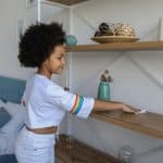 A girl clean her house by wipes shefl